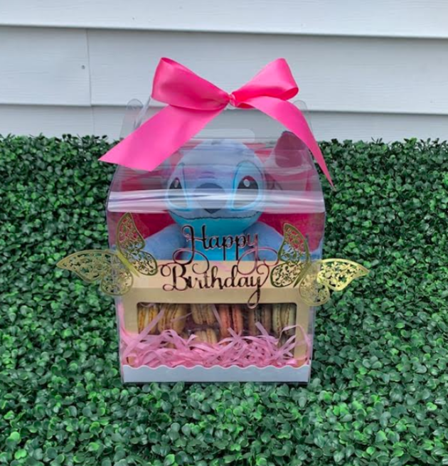 a beautifully crafted birthday surprise box. The first thing you notice is the elegant silk pink bow that adorns the top, adding a touch of sophistication and charm. As you lift the lid, you’re greeted by the delightful sight of a soft, cuddly plush toy, perfect for snuggling and bringing a smile to anyone’s face. Nestled beside the plush toy are an array of colorful, delicious macarons, each one a little work of art. The macarons come in a variety of flavors, from classic vanilla and chocolate to more adventurous options like lavender and pistachio. Their delicate shells and creamy fillings promise a delightful treat with every bite. This birthday surprise box is a perfect blend of sweetness and comfort, making it an unforgettable gift for someone special. 🎁✨